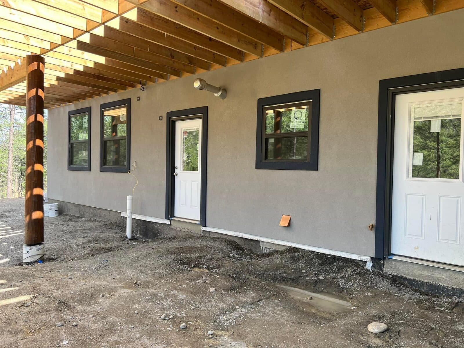 Freshly applied grey stucco on a new-build exterior beneath an exposed timber porch frame