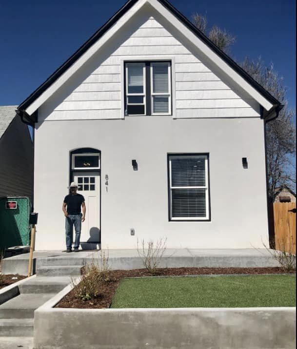 A narrow two-storey city home finished in white stucco with black trim and a new concrete walk