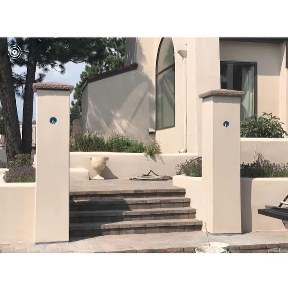 Smooth cream stucco entry columns and low garden walls framing a paved stair to a house entrance